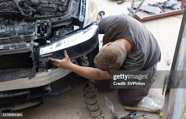 young auto mechanic is repairing a car headlight. - farol estrutura construída imagens e fotografias de stock