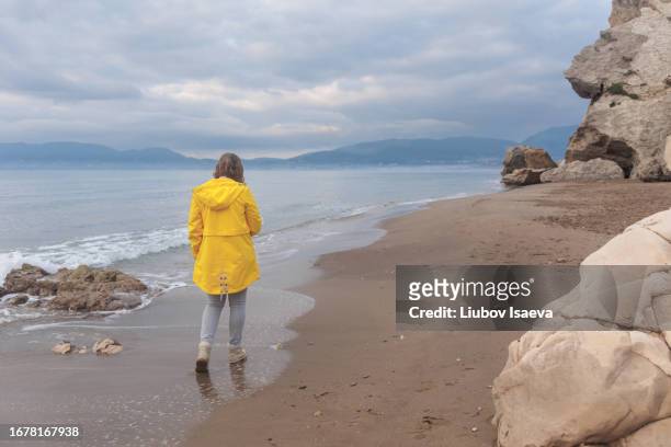 back view of mature woman (40-49 years) walking along sandy beach on gloomy day. - 40 49 years ストックフォトと画像
