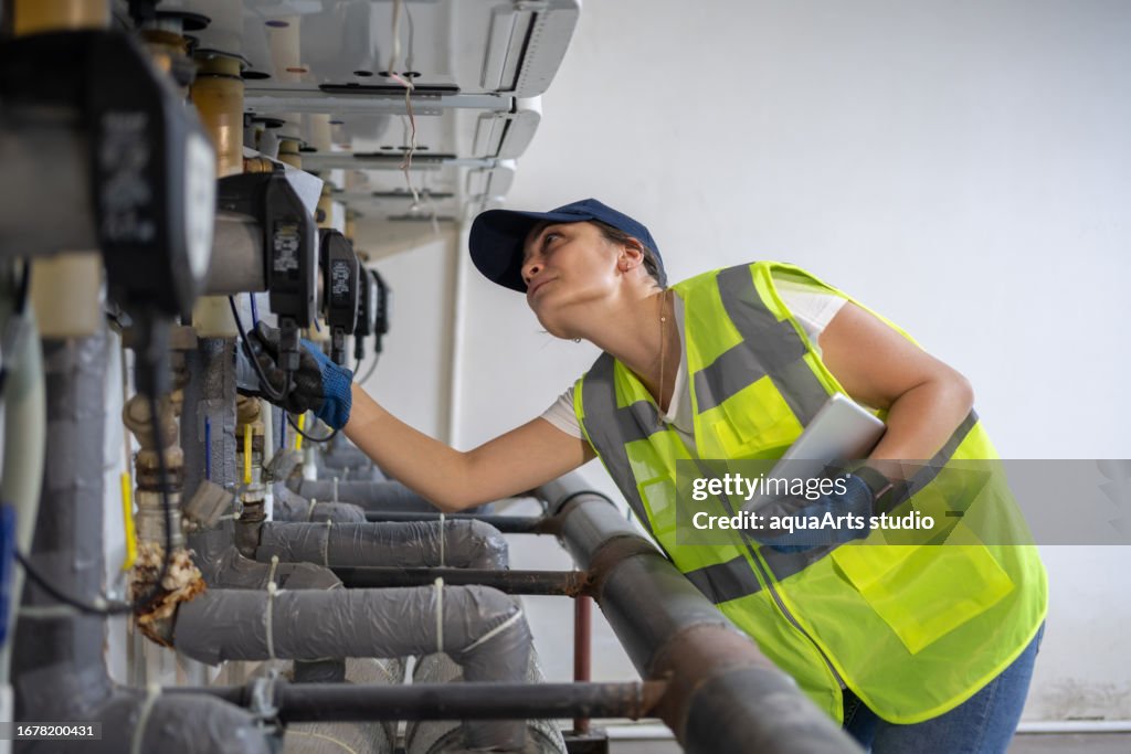 Female Engineer Checking Boiler System In A Basement