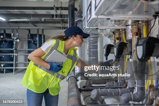 Female Engineer Checking Boiler System In A Basement Female Engineer Checking Boiler System In A Basement