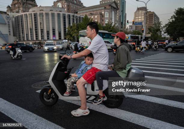 Boy looks towards a shopping small LCD screen as he waits while riding with his parents on a scooter on September 13, 2023 in Beijing, China.