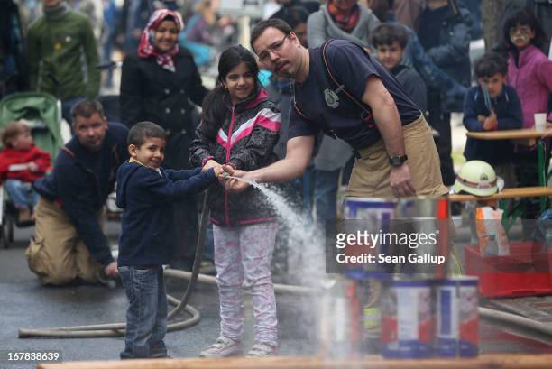 Firemen help children to aim a water hose at stacked cans at the MyFest street food and music fest in immigrant-heavy Kreuzberg district on May Day...