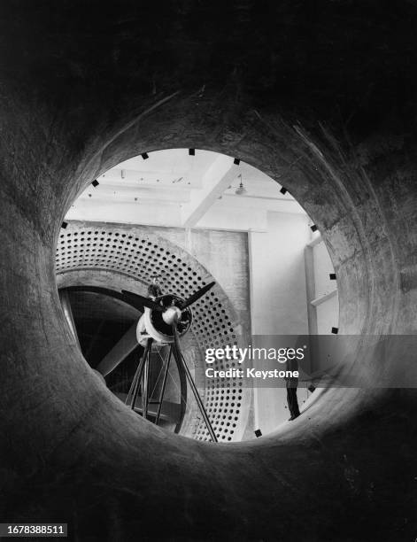 An aviation engineer standing beside an aerial engine on the balance at the entrance of the new wind tunnel ready for the 115 mph test at the Royal...