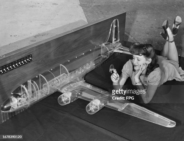 Woman lying on her front beside a clear plastic model of a Douglas C-54 Skymaster military transport aircraft, United States, circa 1945.
