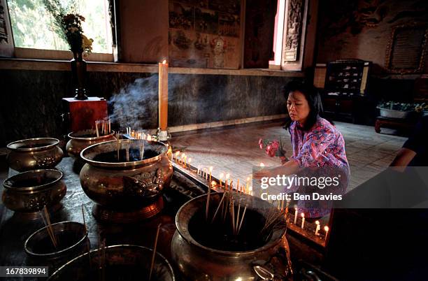 Woman lights joss sticks and makes offerings inside a temple in Nong Khai in the northeast region of Thailand known as Isaan. Scenes like this take...