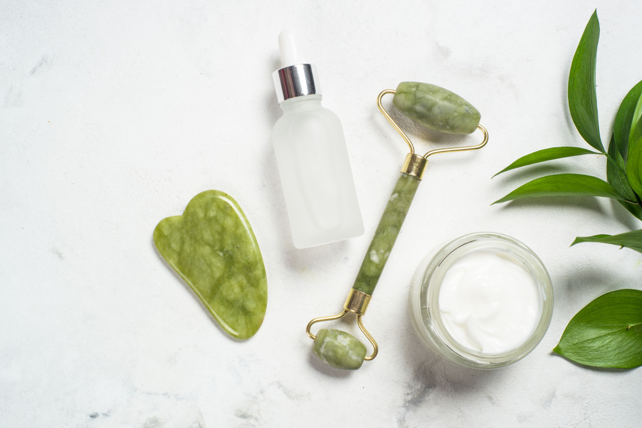 Jade roller and gua sha stone massager with face cream and serum bottle. Jade roller and gua sha stone massager with face cream and serum bottle.