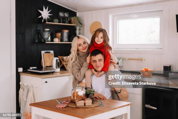 a happy family in red knitted sweaters eat sitting at a table in a cozy kitchen in a country house on a christmas holiday in the countryside. husband wife and daughter spend time together on vacation in december in winter at home - country christmas fotografías e imágenes de stock