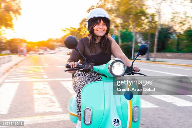 happy latin woman using a sharing system riding a electric moped in barcelona with golden light. - moped stock-fotos und bilder