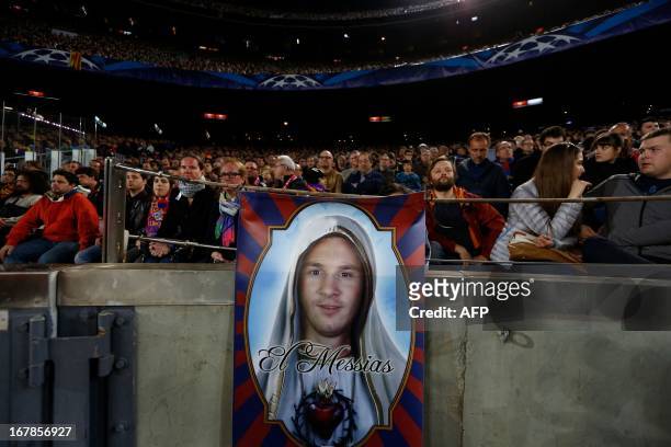 Supporters sit in the stands behind a poster depicting Barcelona's Argentinian forward Lionel Messi as the Messiah during the UEFA Champions League...