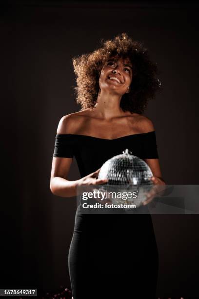 young woman holding a disco ball against dark gray background - woman little black dress stock pictures, royalty-free photos & images