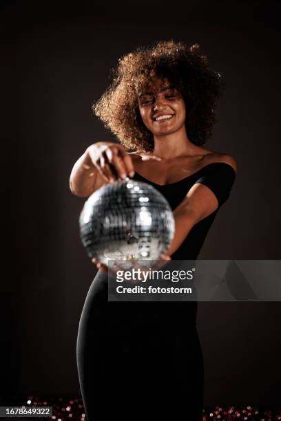 young woman holding a disco ball against dark gray background - black dress party stockfoto's en -beelden