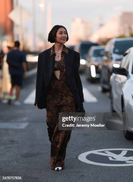 Liz Uy is seen wearing silver necklaces, a black oversized blazer with shoulder pads, underneath black/brow floral pattern matching two-piece in...