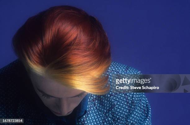 Photo of English Rock musician and actor David Bowie as he looks down, his orange hair offset against the blue background, Los Angeles, California,...