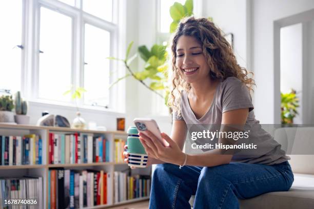 frau zu hause blick auf social media auf ihrem handy beim kaffeetrinken - thermo becher stock-fotos und bilder