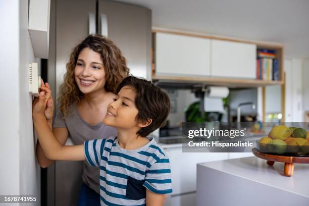 mother and son adjusting the temperature of their house - air conditioner family stock pictures, royalty-free photos & images