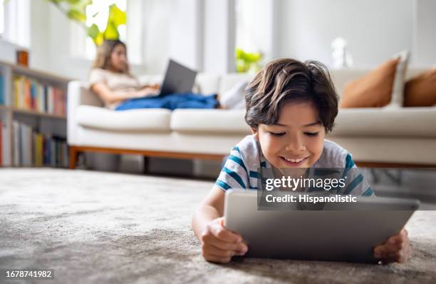 boy watching videos on a digital tablet while his mother is working on her laptop - streaming service stock pictures, royalty-free photos & images