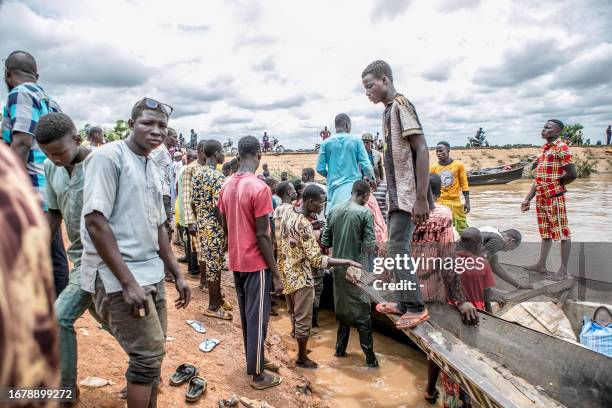 Passengers gather near informal motorised canoes ready to ferry passengers across the River Niger that divides Benin and Niger in the town of...