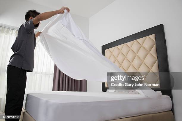 male housekeeper in hotel throwing sheet on bed - bedclothes stockfoto's en -beelden