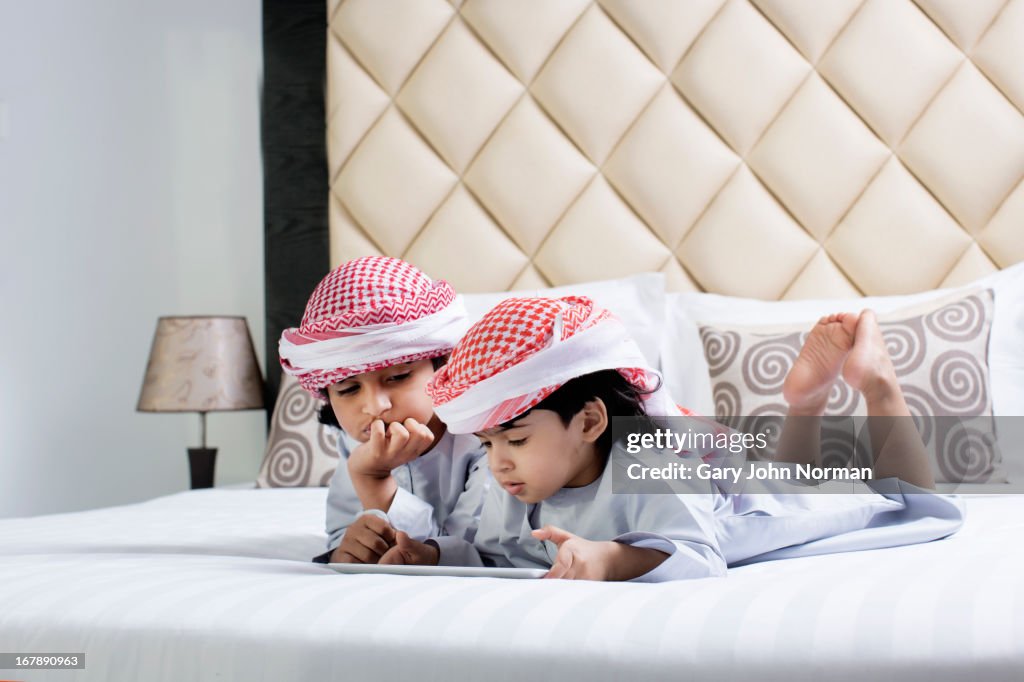 Two Arab boys in traditional dress lay on bed