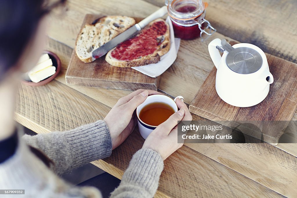 Overhead shot woman holding cup of tea with bread