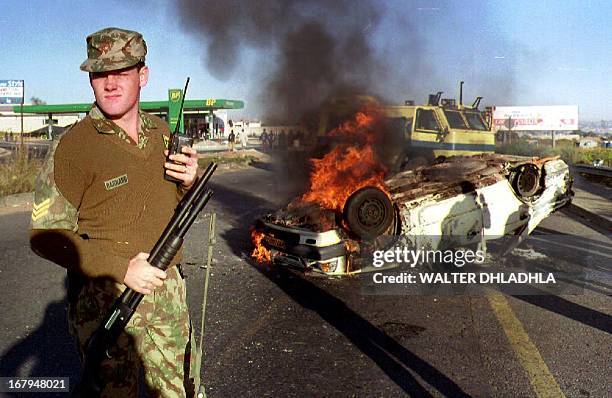 South African policeman stands 19 April 1993 near a burning squad car outside Soweto after it was set alight by an angry mob protesting the...