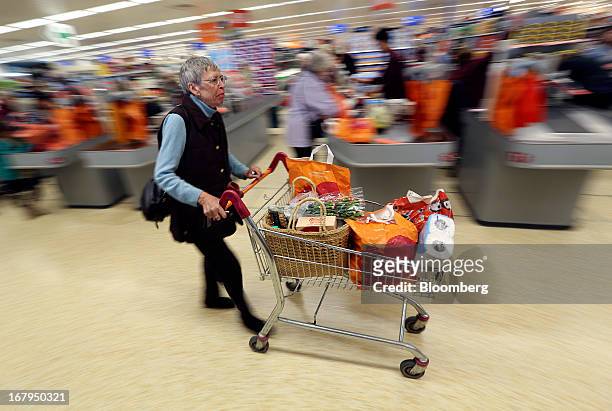 Customer pushes a shopping cart past checkout desks after paying for goods at a Sainsbury's supermarket store, operated by J Sainsbury Plc, in...