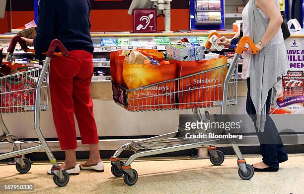 Customers wait with loaded shopping carts at a lottery and cigarette kiosk inside a Sainsbury's supermarket store, operated by J Sainsbury Plc, in...