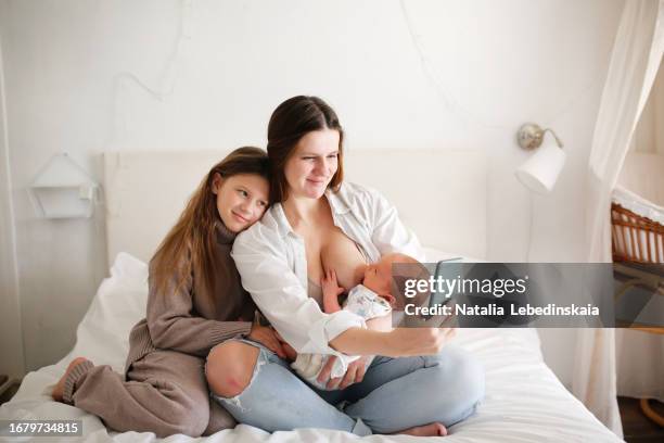 family bonding: mom, baby, and eldest daughter in a smartphone moment. - mother and daughter making the bed stock pictures, royalty-free photos & images