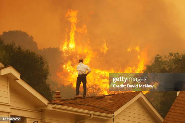 Man on a rooftop looks at approaching flames as the Springs fire continues to grow on May 3, 2013 near Camarillo, California. The wildfire has spread...