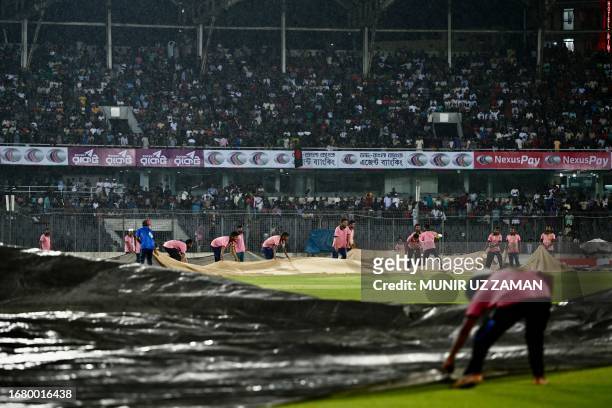 Ground staff cover the field after rain stopped the play during the first one-day international cricket match between Bangladesh and New Zealand at...