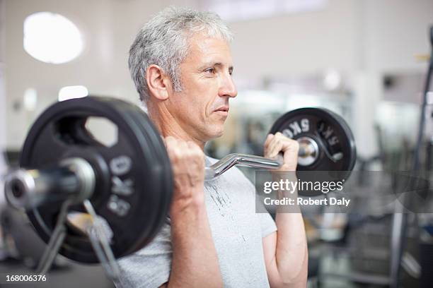 retrato de hombre sonriente sosteniendo barra para pesas en el gimnasio - hombres maduros fotografías e imágenes de stock