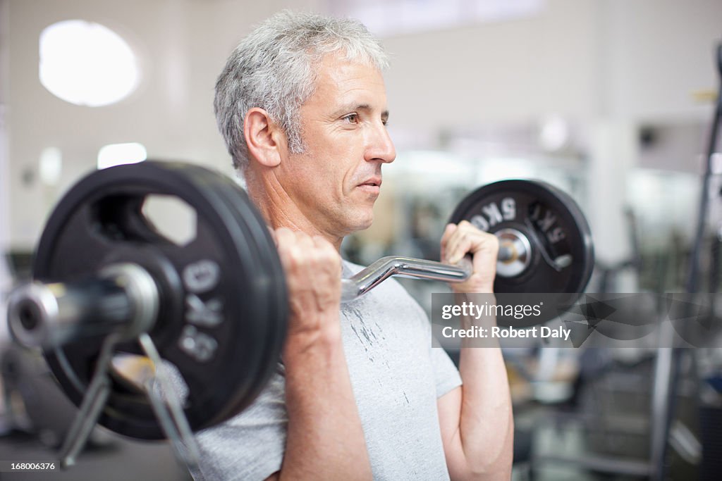 Retrato de homem sorridente segurando barra na academia de ginástica