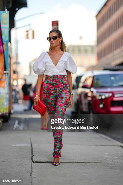 Guest wears sunglasses, earrings, a white v-neck low neck ruffled and gathered puff sleeves white top, high waist gathered floral print pink and...