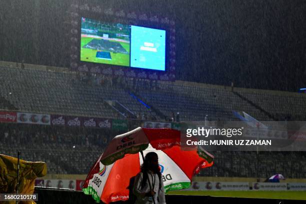 Man takes shelter under an umbrella after the first one-day international cricket match between Bangladesh and New Zealand called off due to rain at...
