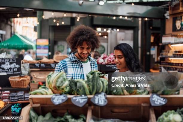 a couple look at the fruit and vegetables on a market stall. - market stall stock pictures, royalty-free photos & images