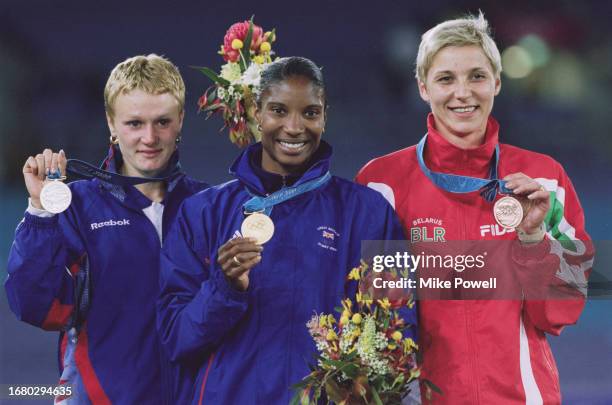 Denise Lewis from Great Britain stands on the victory podium holding the gold medal beside silver medalist Yelena Prokhorova from Russia and bronze...