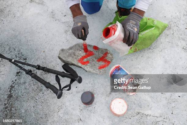 Rupert Schwarzl, a team member with scientists from the University of Graz, paints a number and survey dot used for GPS recording onto a flat stone...