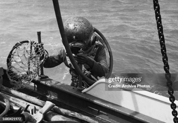 Pearl diver wearing a diving helmet climbs aboard their boat during a pearl diving expedition, off the coast of Australia, circa 1955.
