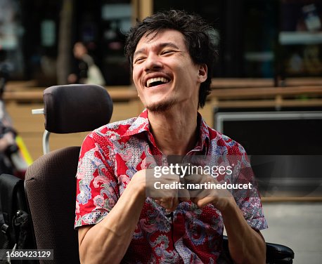 Young man with cerebral palsy laughing outdoors in city. Young man with cerebral palsy laughing outdoors in city.