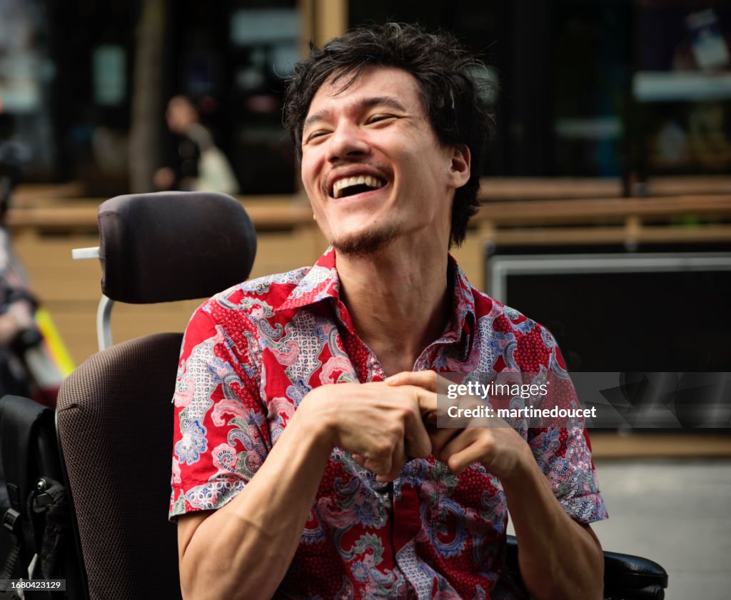 Young man with cerebral palsy laughing outdoors in city.
