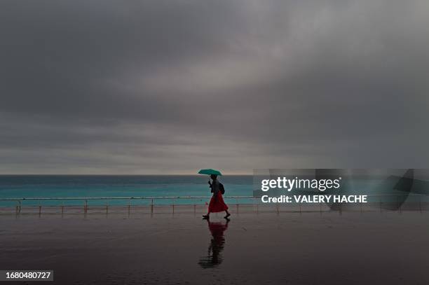 Woman shelters from heavy rainfall with an umbrella as she walks along the "Promenade des Anglais" on the French riviera city of Nice, on September...