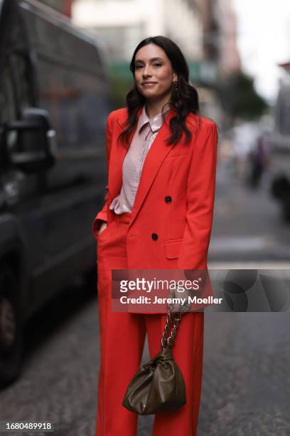 Fashion Week guest is seen wearing golden earrings, a red matching two-piece consisting of an unbuttoned blazer with shoulder pads and wide suit...