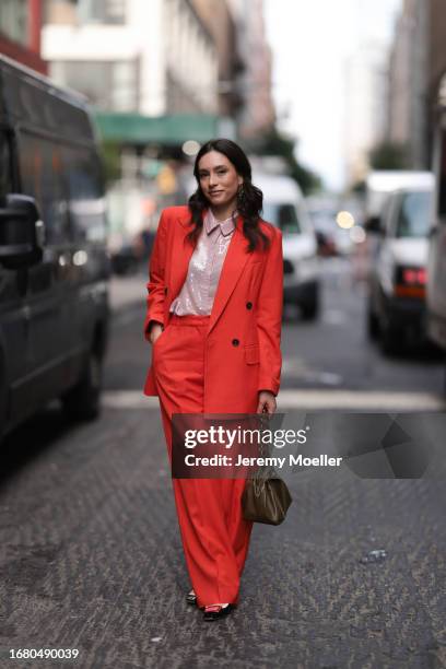 Fashion Week guest is seen wearing golden earrings, a red matching two-piece consisting of an unbuttoned blazer with shoulder pads and wide suit...