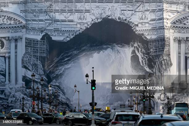 People drive past an installation by French artist JR, depicting the philosophical allegory of Plato's cave, covering part of the facade of the Opera...