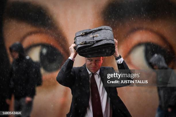 Man protects himself from heavy rains with his briefcase as he walks past a reproduction of "Portrait of a man" by Italian painter Antonello da...
