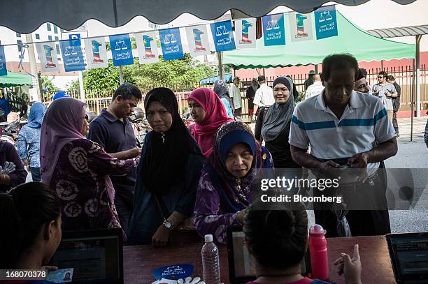 Volunteers for the ruling Barisan Nasional coalition, seated foreground, assist voters with queries outside a polling station for the general...