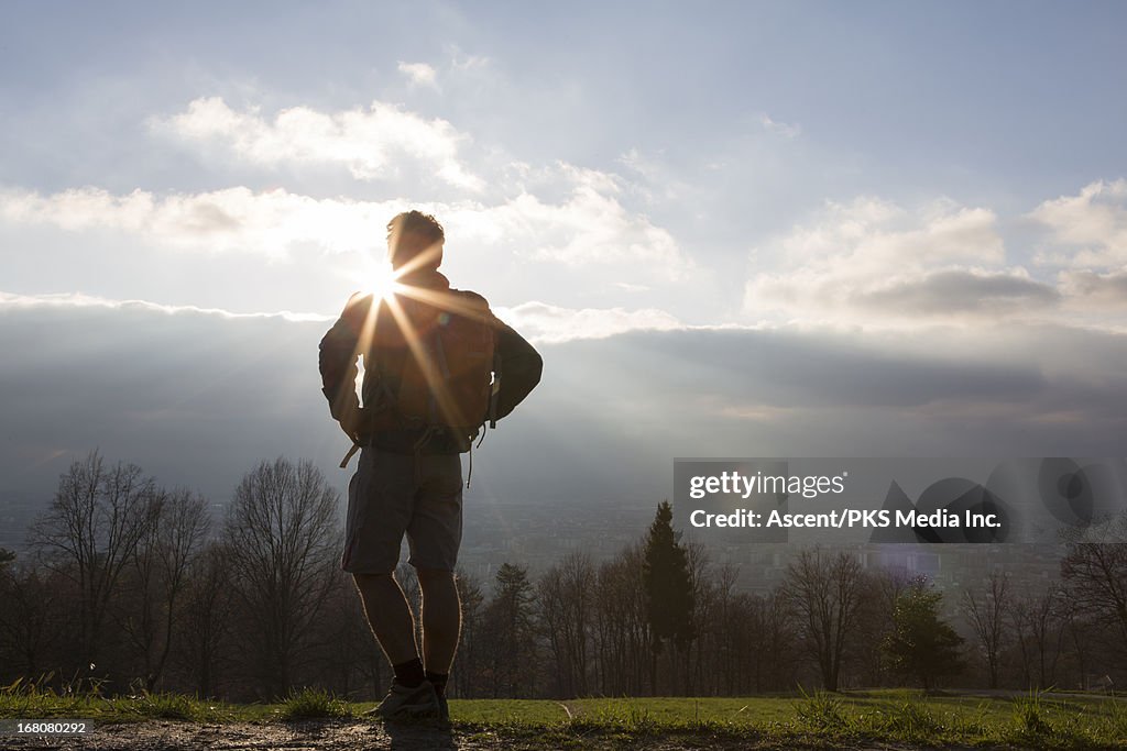 Hiker stands on hill above city, looks to sunrise