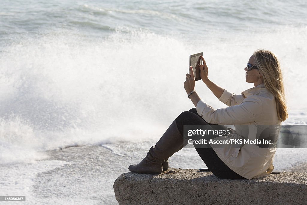 Woman takes pic with digital tablet, crashing surf