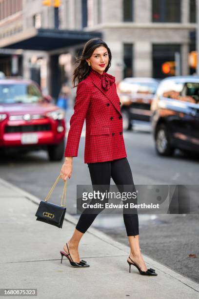 Kate Bartlett wears a headband, a red and black checkered bow tie, double breasted blazer jacket, black cropped leggings, a black leather bag, a...