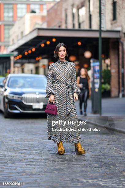 Heart Evangelista wears golden earrings, a houndstooth pattern printed midi pleated dress, a burgundy leather bag from Carolina Herrera, golden...